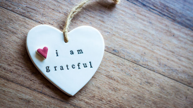 A heart shaped sign showing i am grateful on a wooden surface
