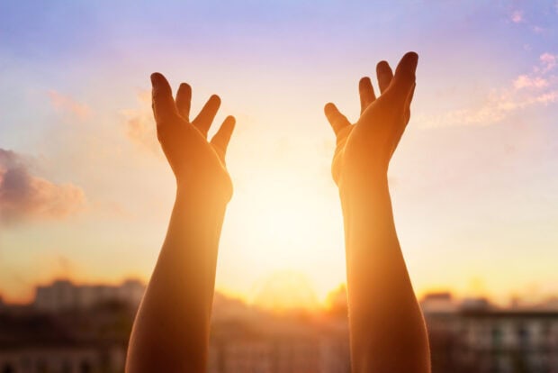 Hands reaching out to the sky expressing gratitude at sunrise in a peaceful city scene