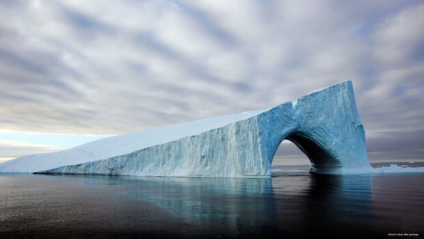 A large iceberg with an arch shape floating in calm waters of Greenland