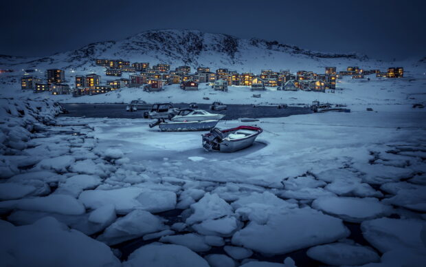 Small boats are frozen in icy water near Greenland town at dusk