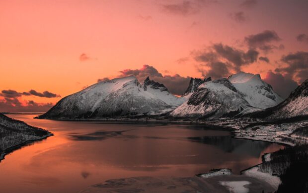 Snowy mountains in Greenland under a vibrant orange sky reflecting on calm water