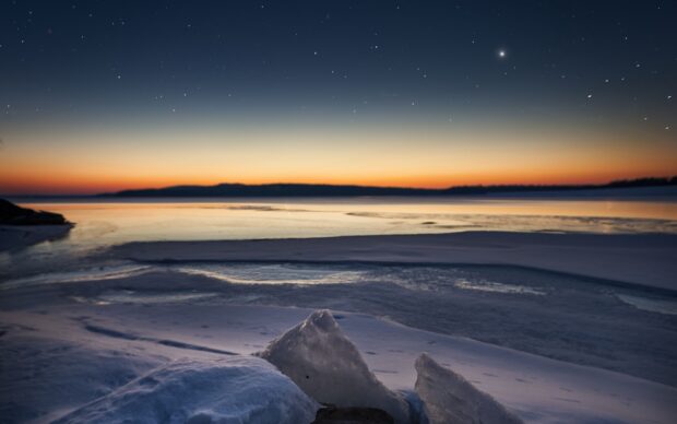 Clear night sky over frozen Greenland coast with ice formations and distant horizon