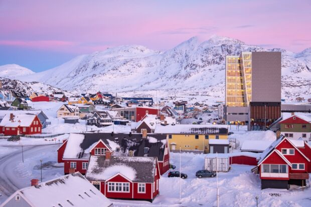 Colorful Greenland houses covered with snow under a pink sky and snowy mountains in Greenland