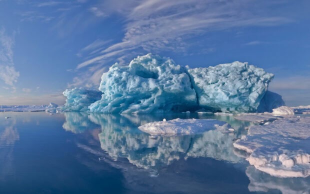 Large Greenland ice formation reflecting on calm Arctic water under a blue sky