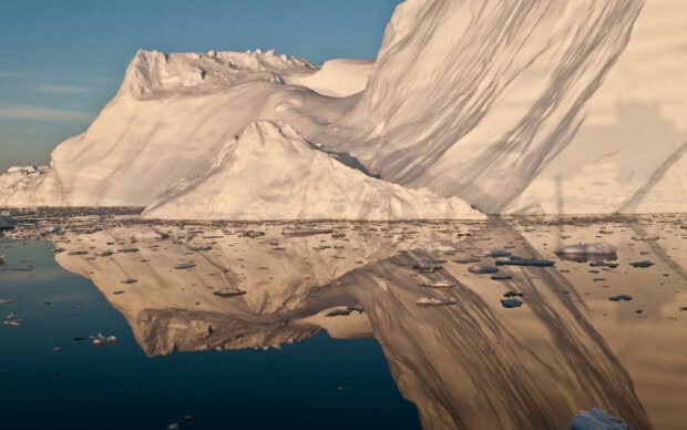 Large iceberg reflections on calm water in Greenland during sunset