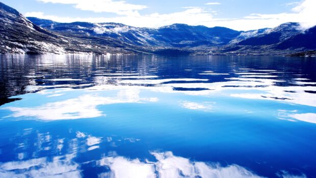 Calm water reflecting mountains and sky in Greenland with vivid blue tones