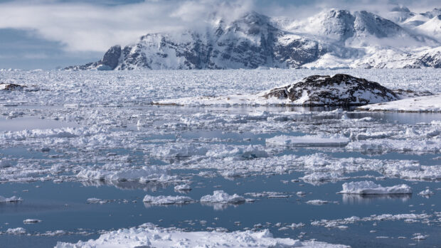 Icy Greenland landscape with snow covered mountains and floating ice in calm blue water