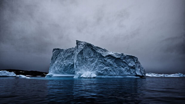 Massive Greenland iceberg floating in dark ocean under cloudy sky