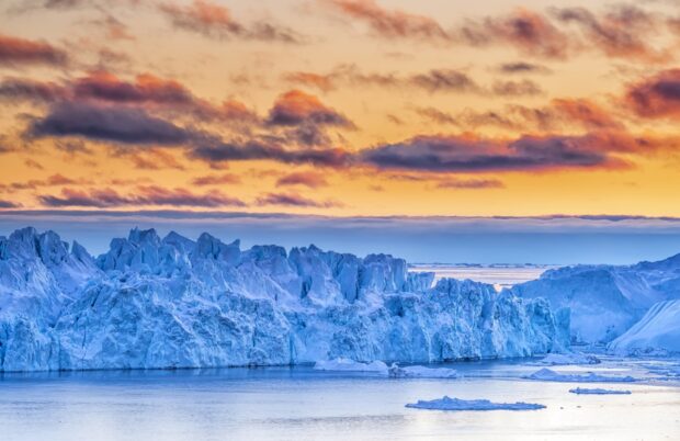 Stunning Greenland ice formations under a colorful sunset sky with calm water in the foreground