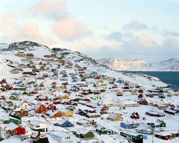 Colorful houses on snowy Greenland landscape with hills and sea in the background