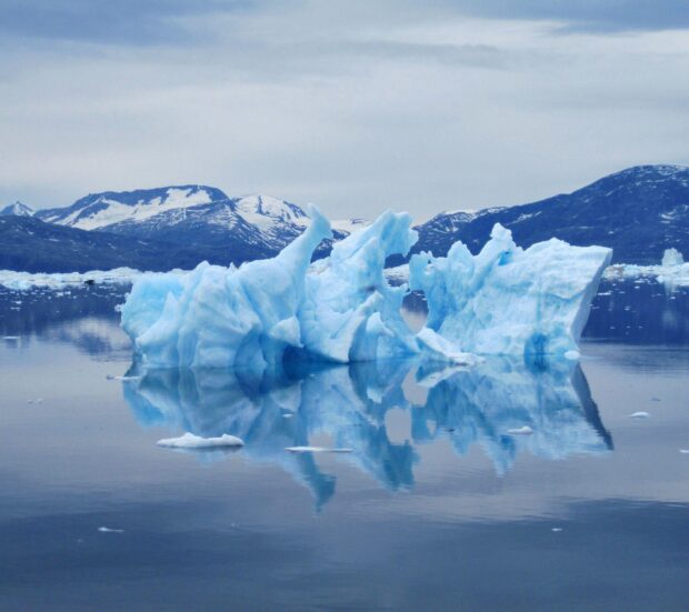 A large iceberg floating in calm water of Greenland with mountains in the background