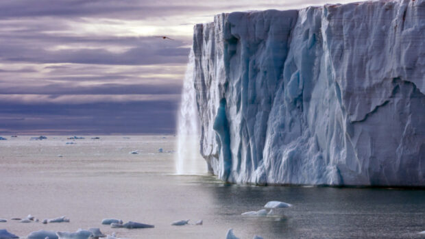 Massive Greenland iceberg dropping water into the sea under cloudy skies