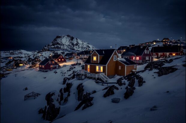 Snow covered village under dark sky in Greenland with warmly lit houses at night