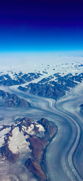 A stunning aerial view of Greenland glaciers winding through mountain ranges under a clear blue sky