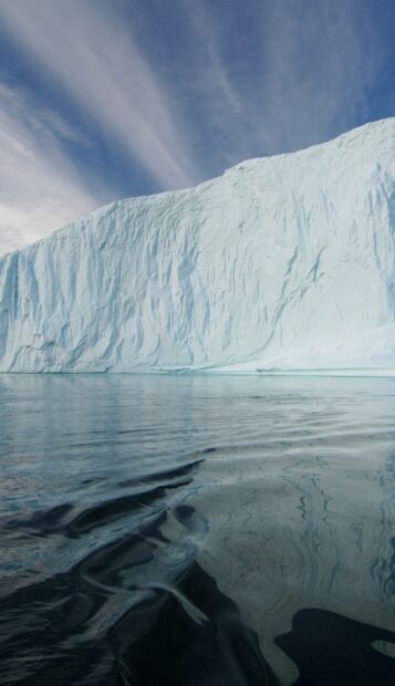Massive glacier in Greenland reflecting on calm water under blue sky