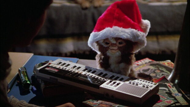 A gremlin wearing a Santa hat playing a keyboard on a desk