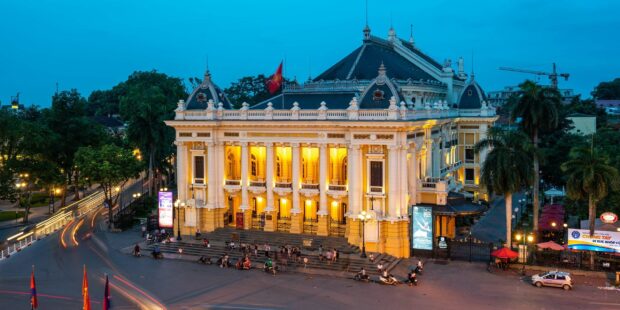 The Hanoi Opera House surrounded by trees and people in the evening light