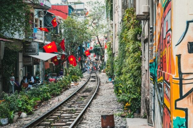 Narrow railway street with Vietnam flags and greenery in Hanoi urban area