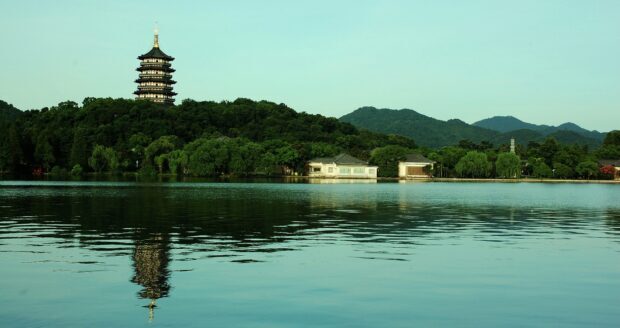 Ancient tower surrounded by lush trees reflected in calm water of Hanoi lake