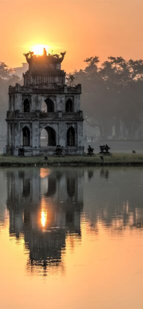 Ancient tower in Hanoi reflecting in water during sunrise with calm atmosphere