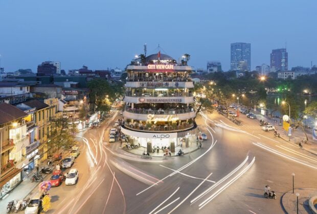 Hanoi street with iconic round building and moving traffic lights at dusk