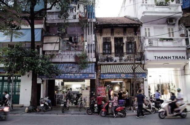 Old Hanoi street shopfronts with motorbikes and pedestrians in urban life