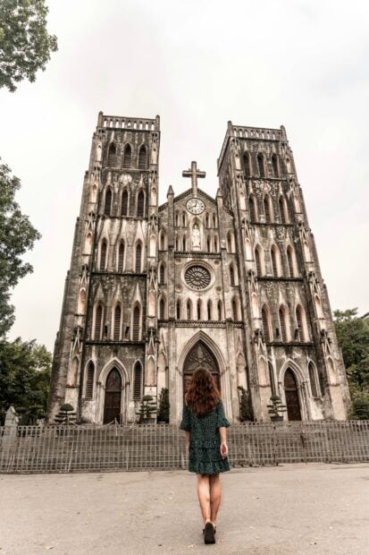 A woman admiring historic cathedral architecture in Hanoi with detailed stonework and tall towers