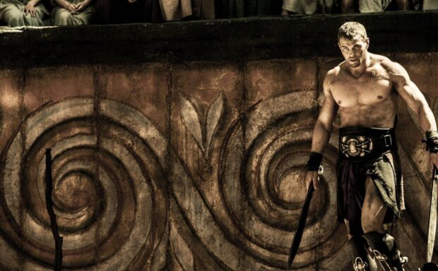 Muscular Hercules warrior holding swords in ancient arena with spiral stone wall background
