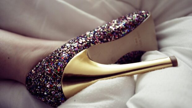 A glittery high heels shoe with a golden stiletto heel resting on a soft surface