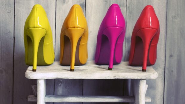 Four colorful high heels arranged on a wooden stool with a rustic background