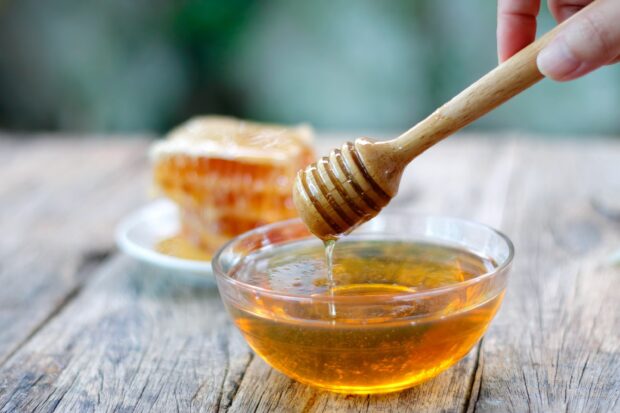 A honey dipper dripping honey into a bowl of golden honey on a wooden surface