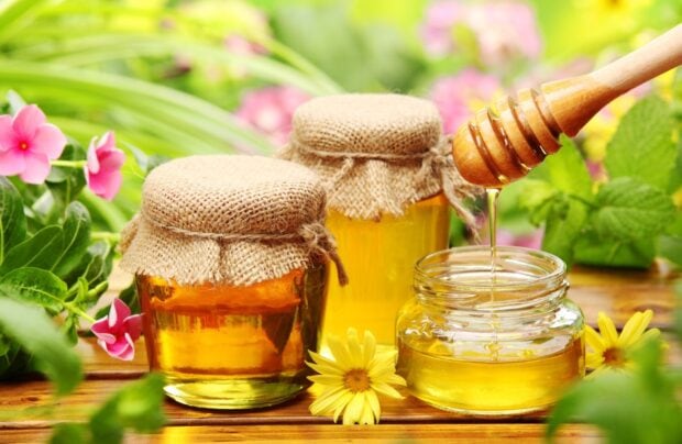 Two jars of honey with natural flowers around on wooden table