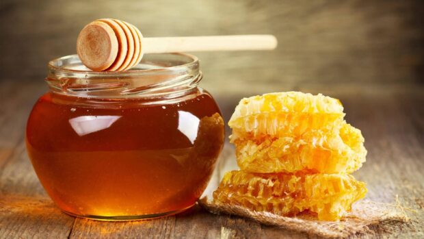 A jar of honey with honeycomb pieces on a wooden surface showing natural honey textures