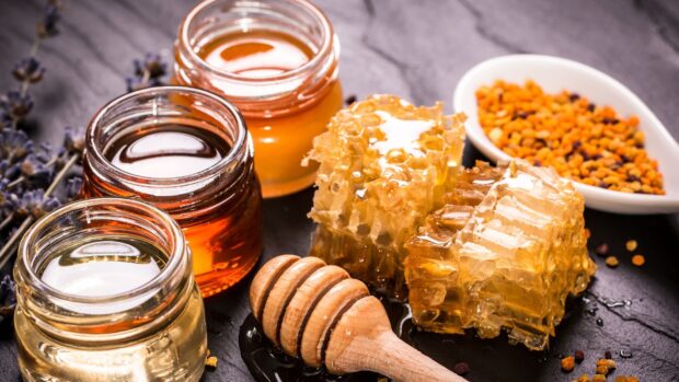 Close up of honey with honeycomb and jars on black slate surface