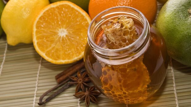 Honeycomb with citrus fruits and spices displayed in a glass jar on a bamboo mat