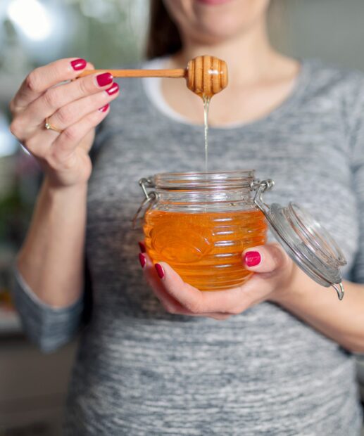 A woman holding honey dripping from a honey dipper into a jar of honey