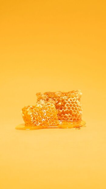 Close up of natural honeycomb dripping with honey on a yellow surface