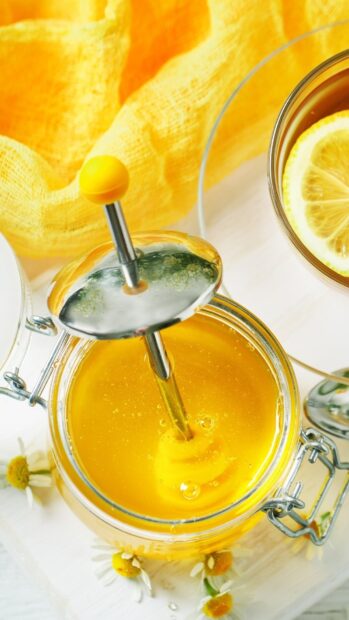 Golden honey in jar with honey dipper near chamomile flowers