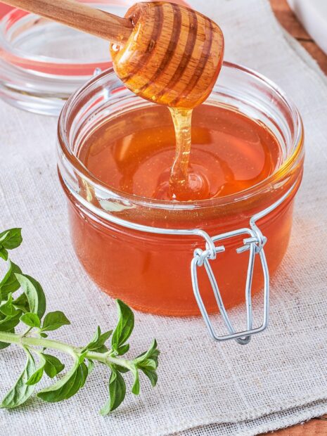 Honey dripping from a wooden dipper into a jar of fresh honey