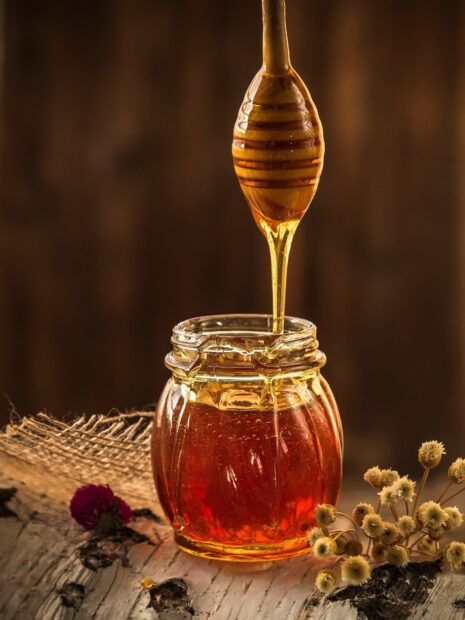 Honey dripping from a wooden dipper into a jar of golden honey