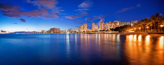 A stunning Honolulu cityscape with high rise buildings and calm ocean at twilight