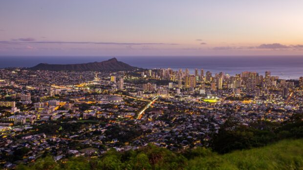 A vibrant cityscape showcasing Honolulu at dusk with illuminated buildings and Diamond Head in the background