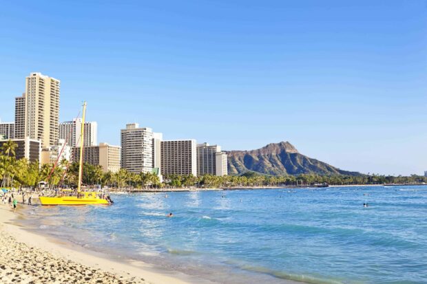 A vibrant view of Honolulu city skyline and Diamond Head mountain with a yellow sailboat on the beach