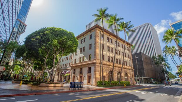 Historic building surrounded by palm trees and Honolulu cityscape in bright daylight