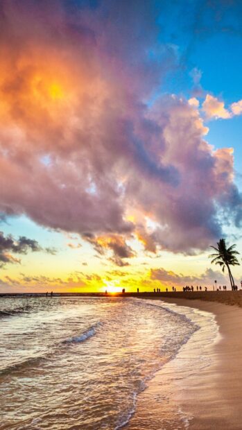 Colorful sunset clouds over Honolulu beach with palm tree and people walking