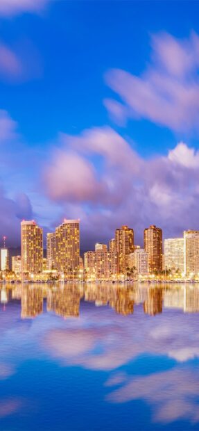 City skyline at Honolulu with high rises reflected in calm water at twilight