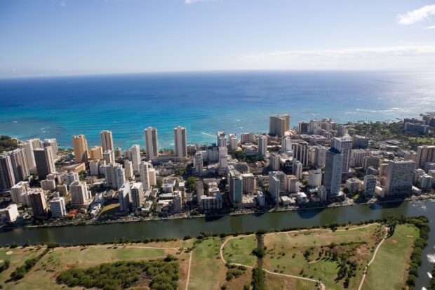 Aerial view of Honolulu cityscape with turquoise ocean and green park in the foreground