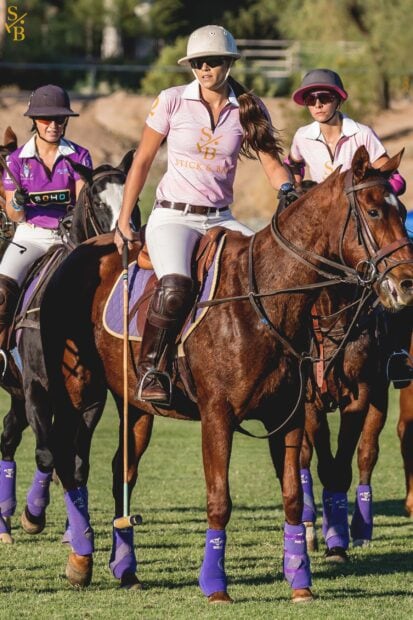 Female horse polo player riding a horse with other players in action on the field