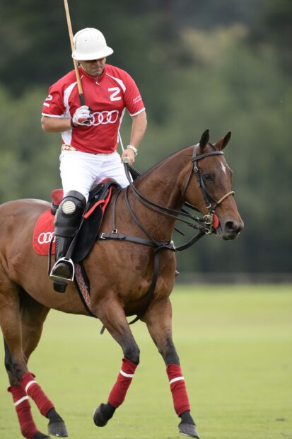 A polo player riding a horse polo on the field with red uniform and white helmet