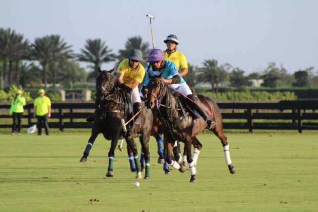 Three horse polo players competing intensely on a green field during a match